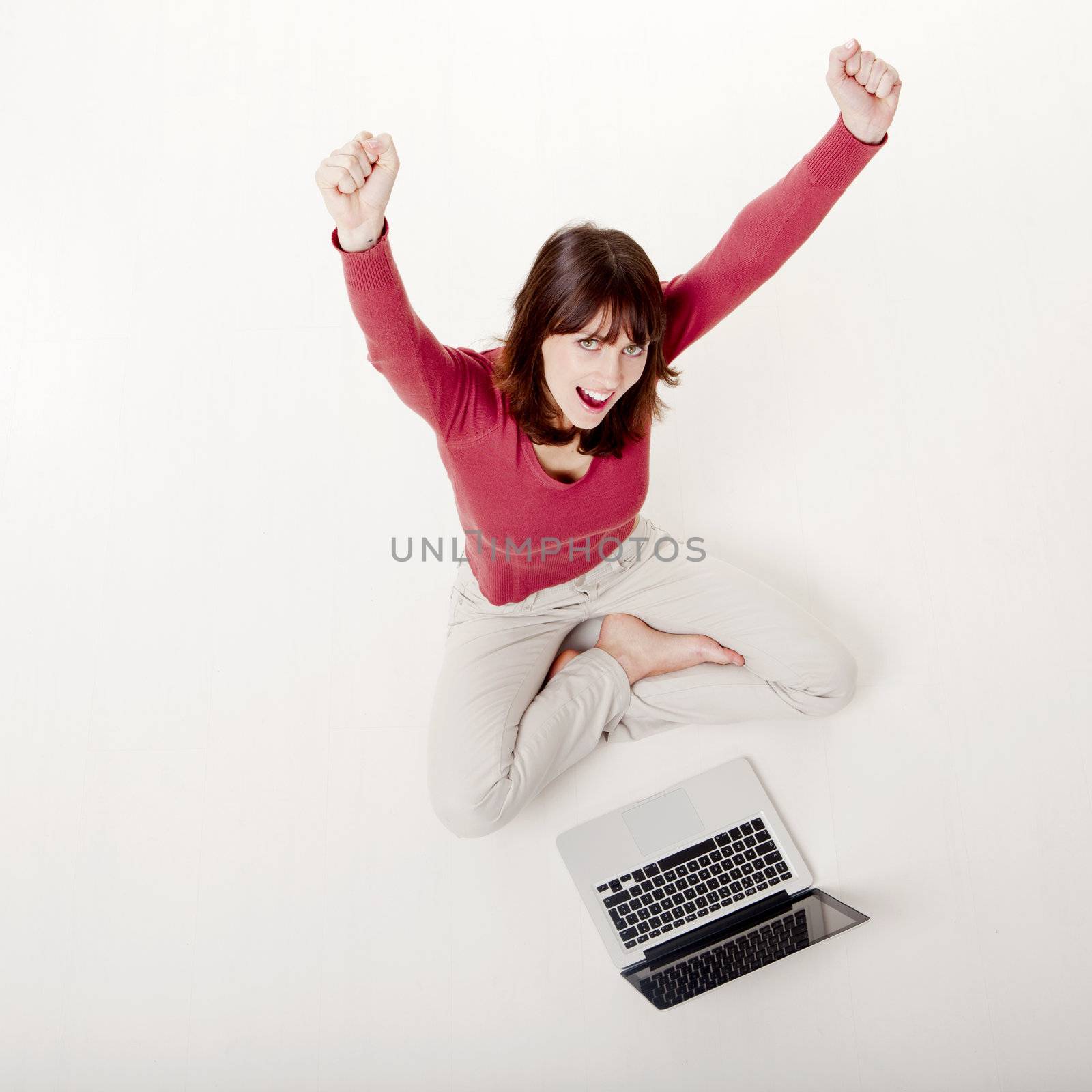 Happy woman with arms raised, sitting on the floor with a laptop