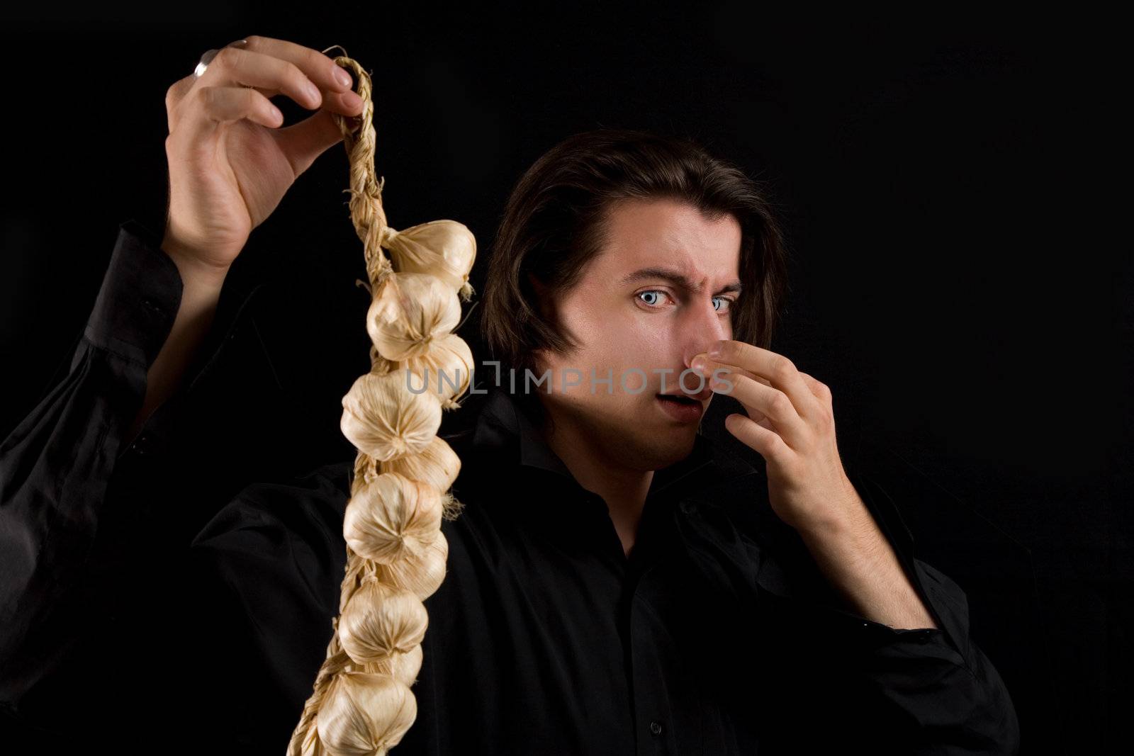 Handsome vampire doesn�t like the smell of garlic, isolated on black background 