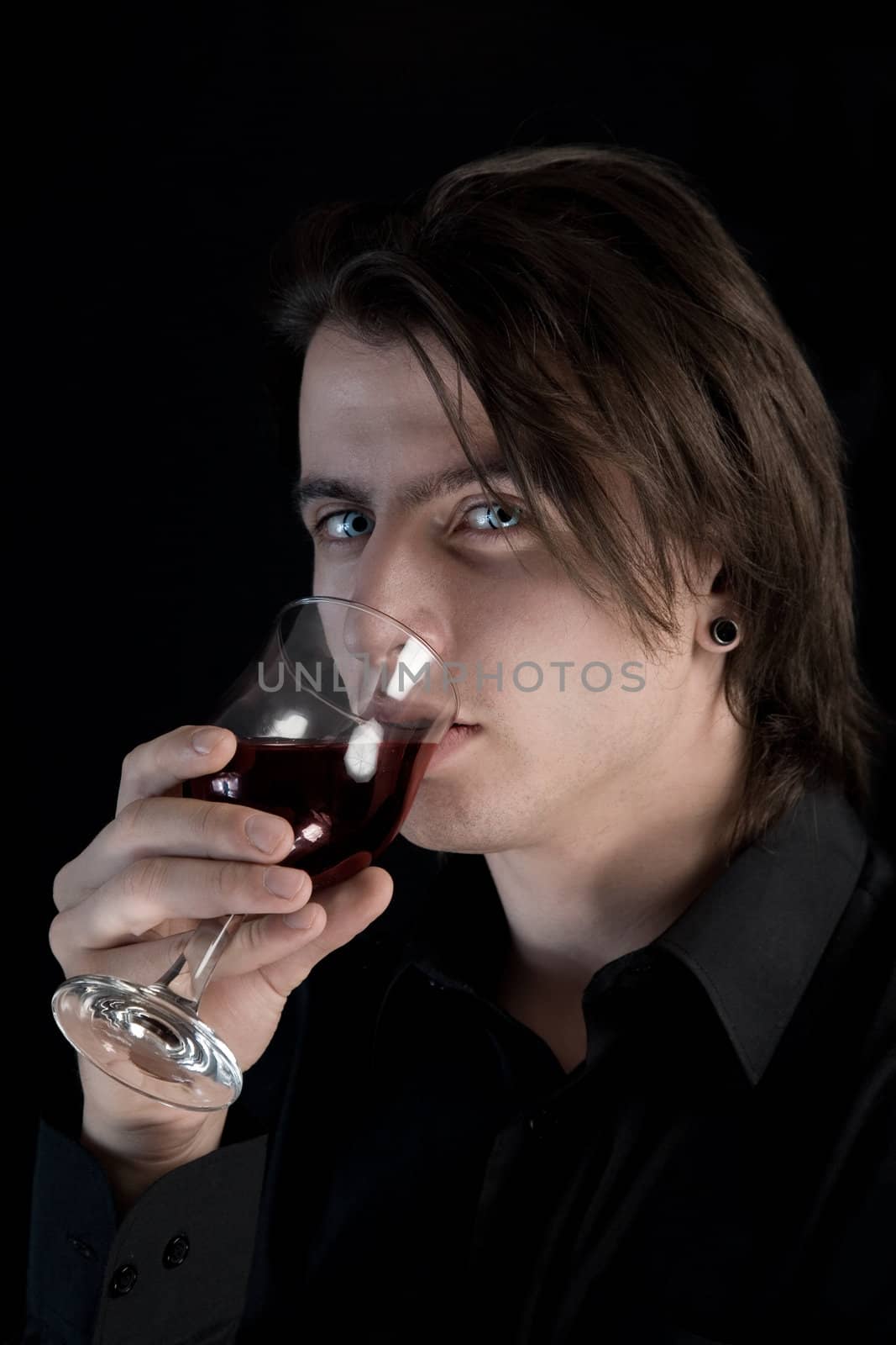 Handsome pale vampire with blue eyes drinking wine or blood, Halloween theme 