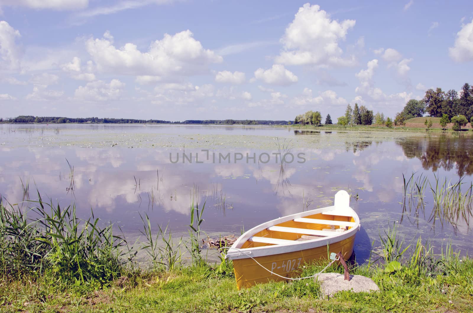 Yellow boat moored at shore. Amazing landscape view of sunset lake with cloudy sky reflections.