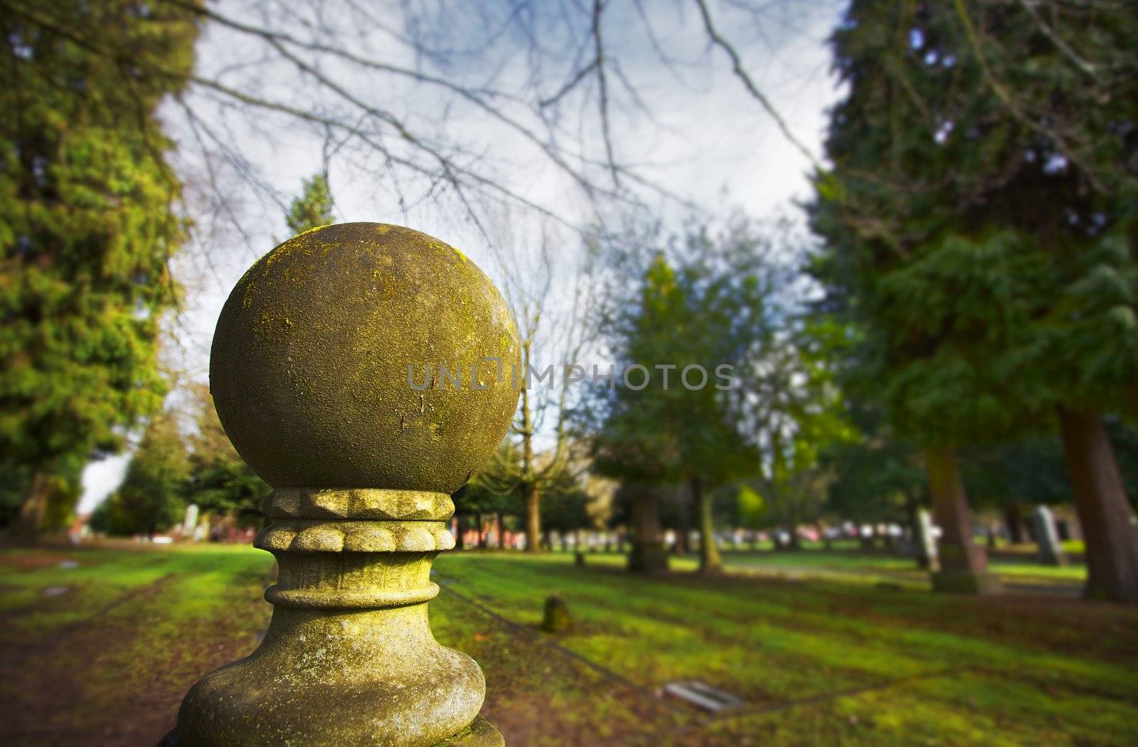 Old weatherd moss covered stone ball sculture with a background of a lawn and trees