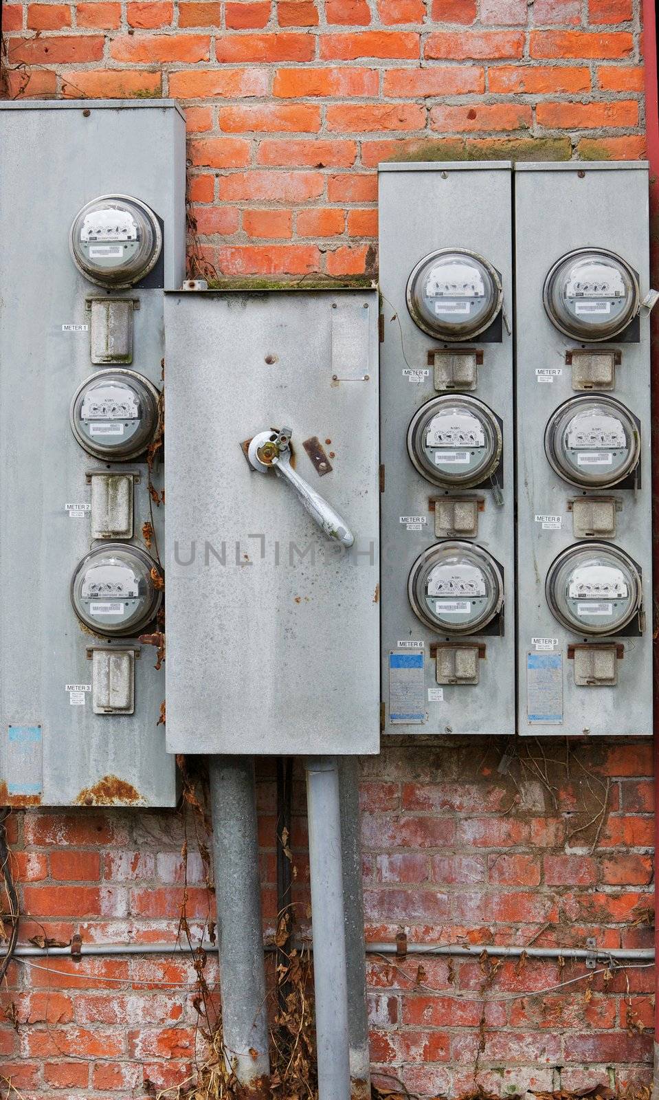 Eight old weathered rusty power meters on a orange and red brick wall