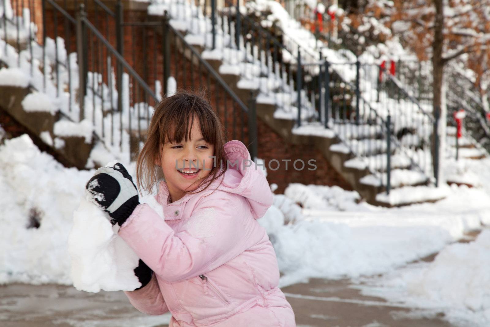 Winter portrait of a smiling little girl playing in the snow throwing a big snow ball.