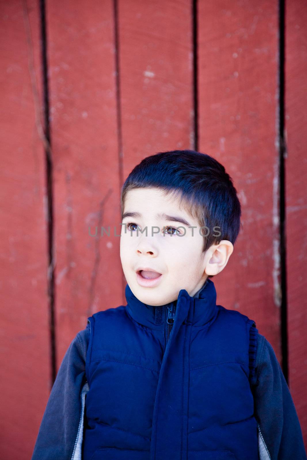Little boy looking up and to the left in front of red textured background with a surprised and amazed expression.