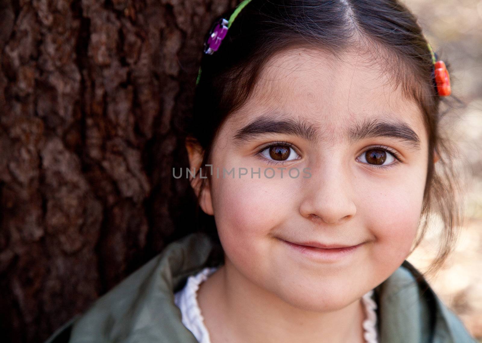 Closeup portrait of a smiling happy little girl in front of a tree with tree bark texture in the background