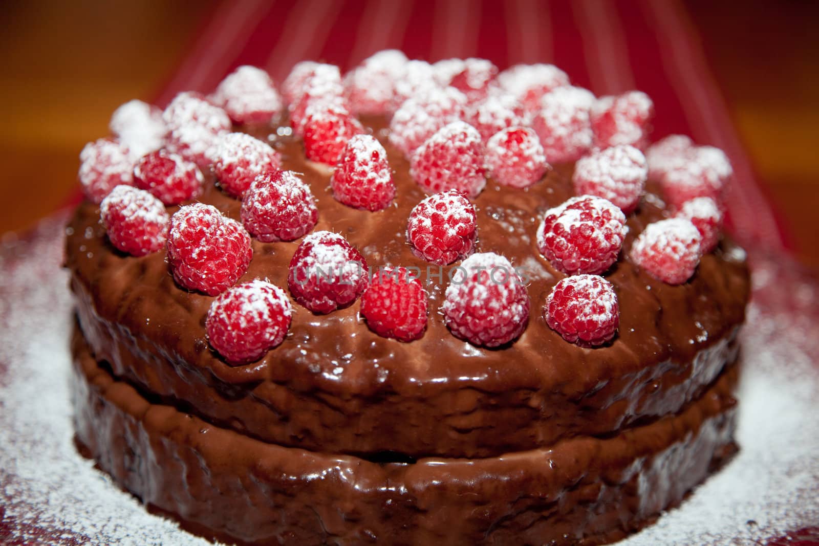 Whole delicious birthday cake with chocolate ganache and raspberries with dusting of powdered sugar.