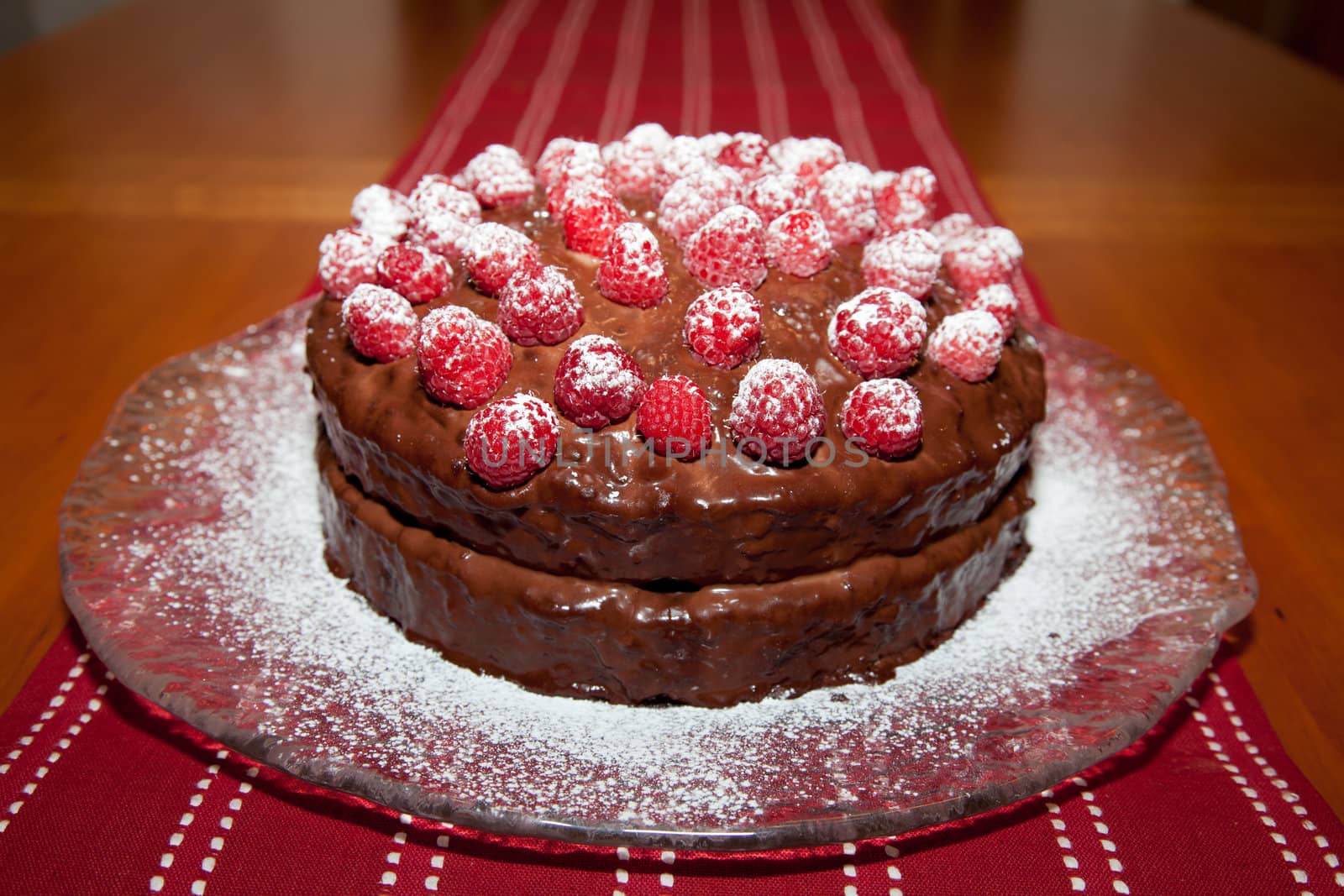 Whole delicious birthday cake with chocolate ganache and raspberries with dusting of powdered sugar.