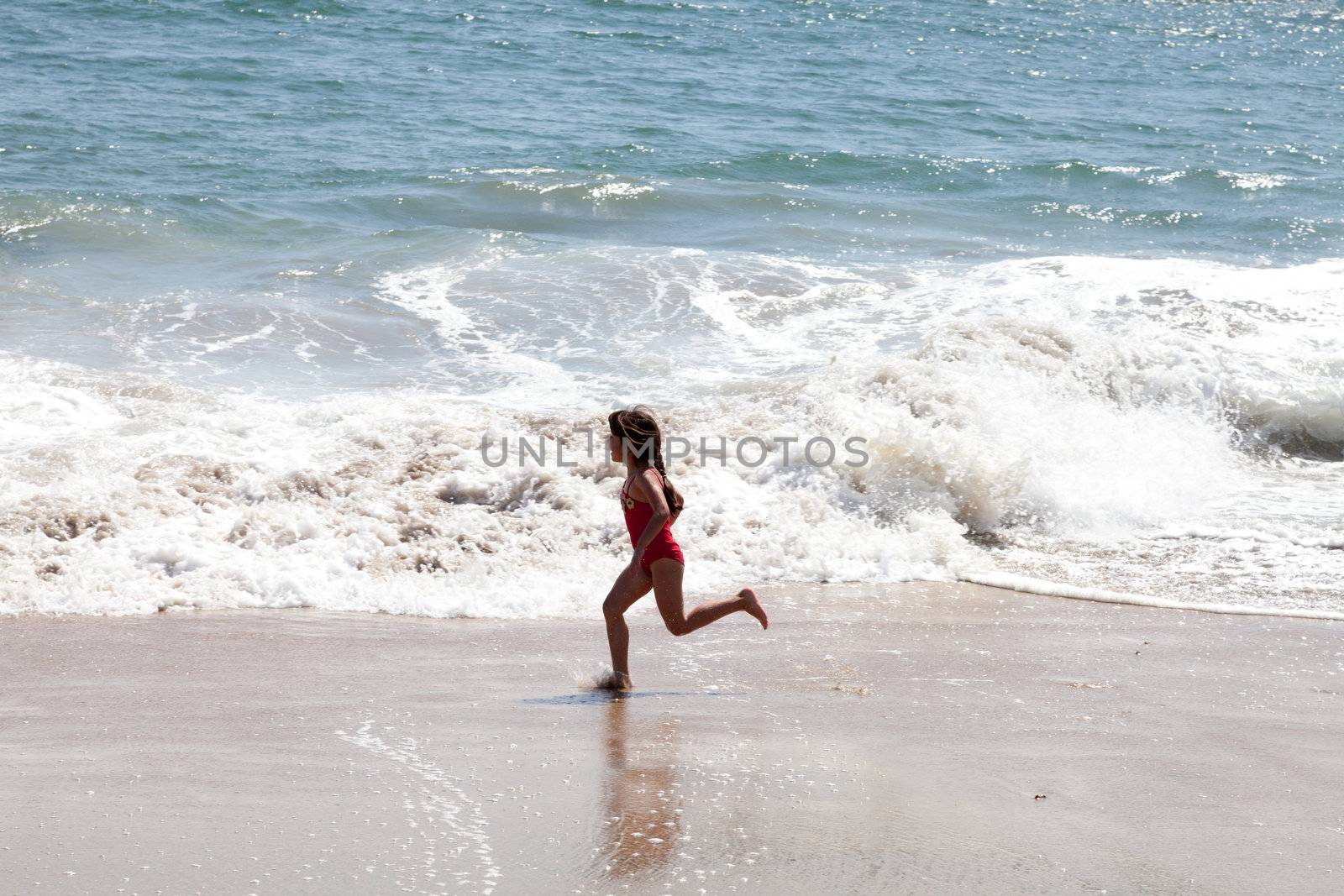 Little girl running and exercising on the beach in the breaking waves.