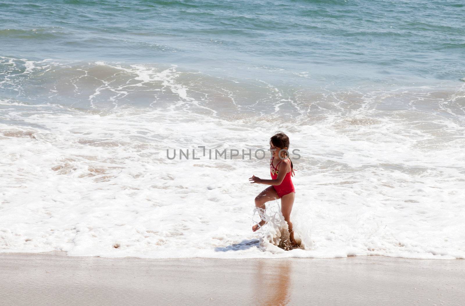 Little girl running and exercising on the beach in the breaking waves.