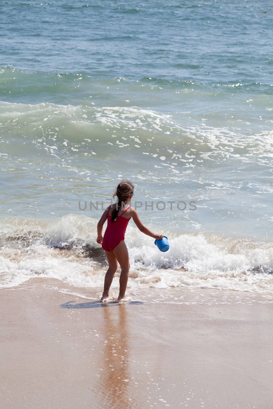 Very excited little girl running in the ocean surf with a blue bucket