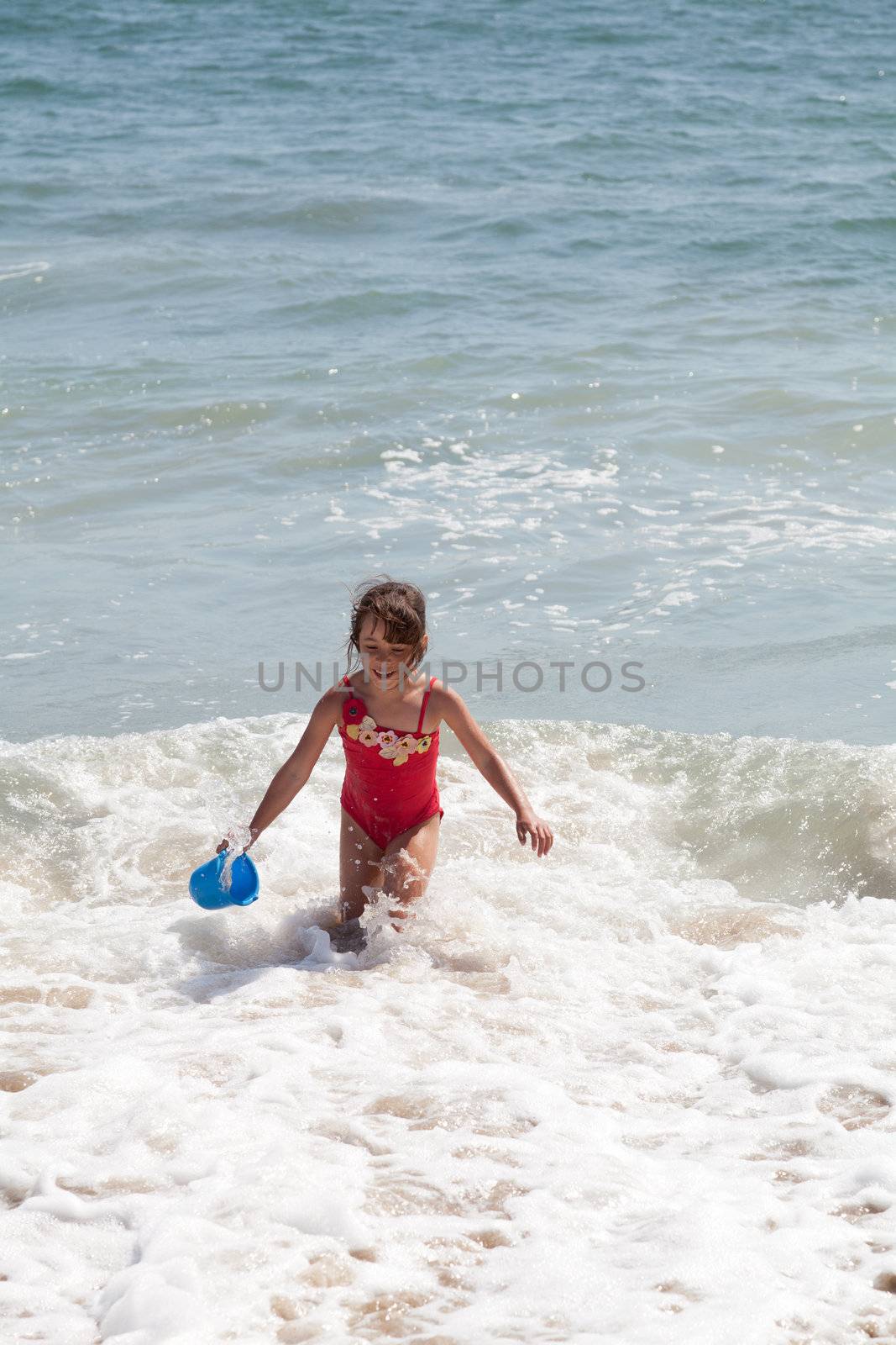 Very excited little girl running in the ocean surf with a blue bucket