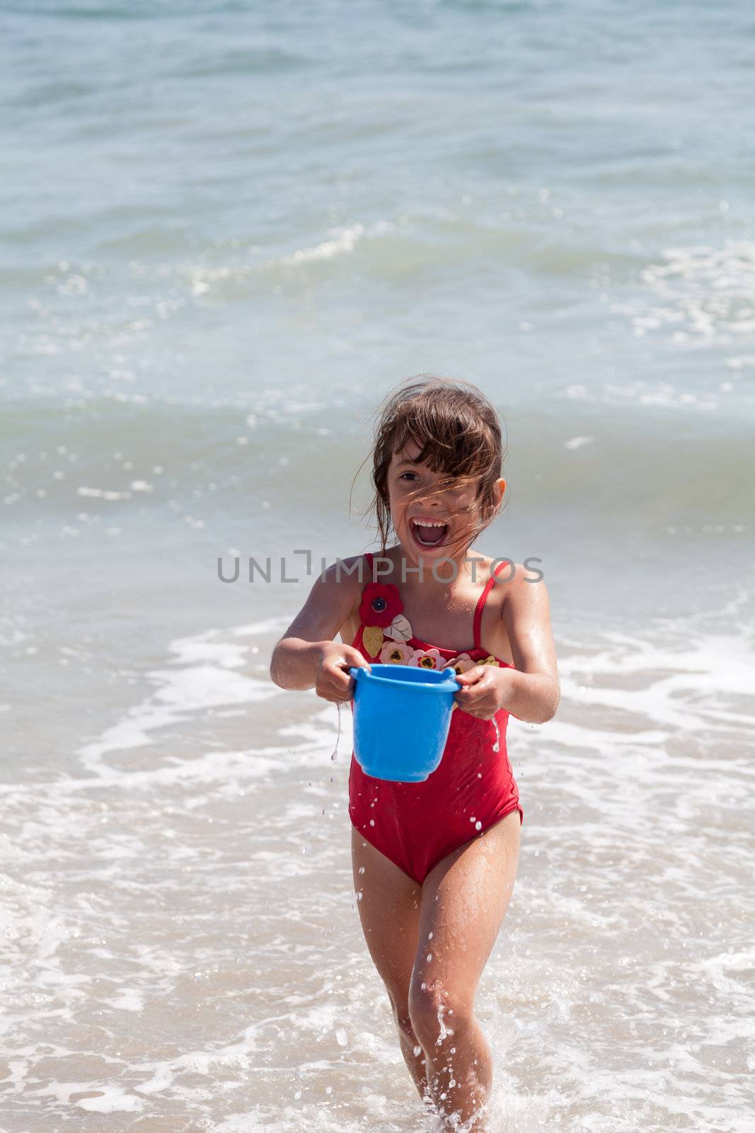 Very excited little girl running in the ocean surf with a blue bucket