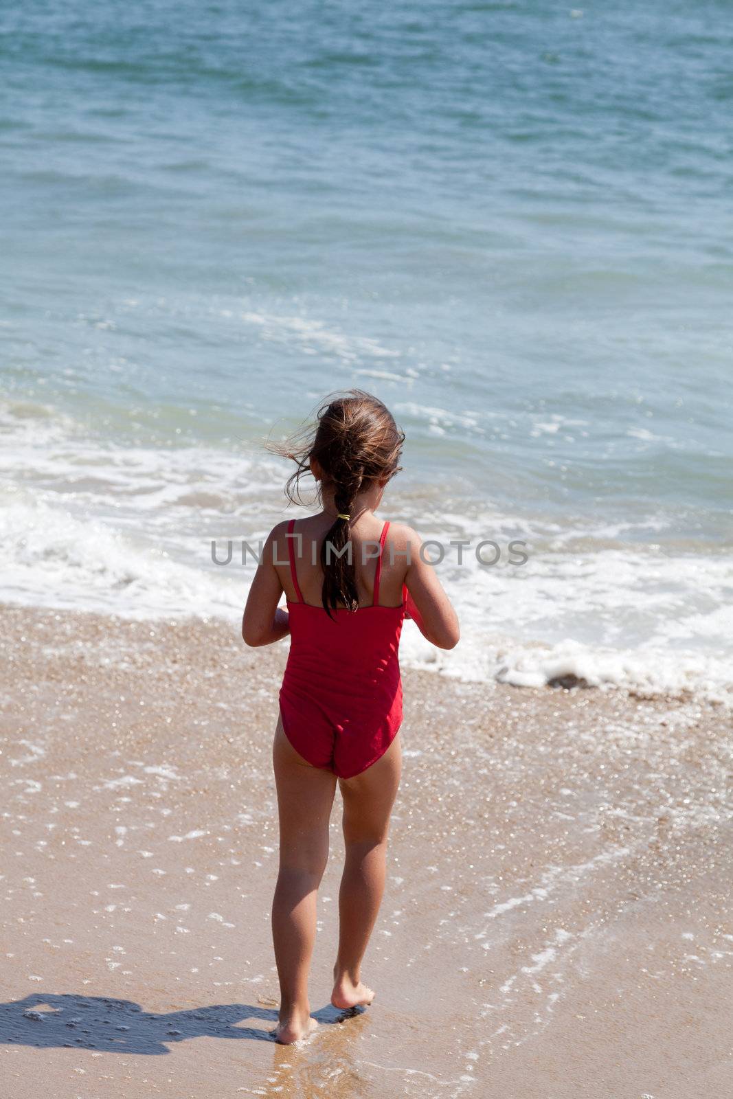 Little girl playing on the beach walking into the ocean surf and waves.