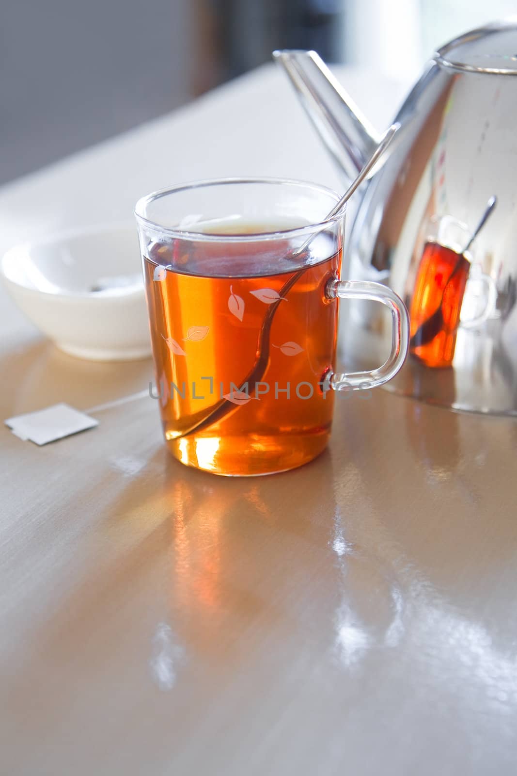 Glass mug with tea, teapot en teabag on table by Colette