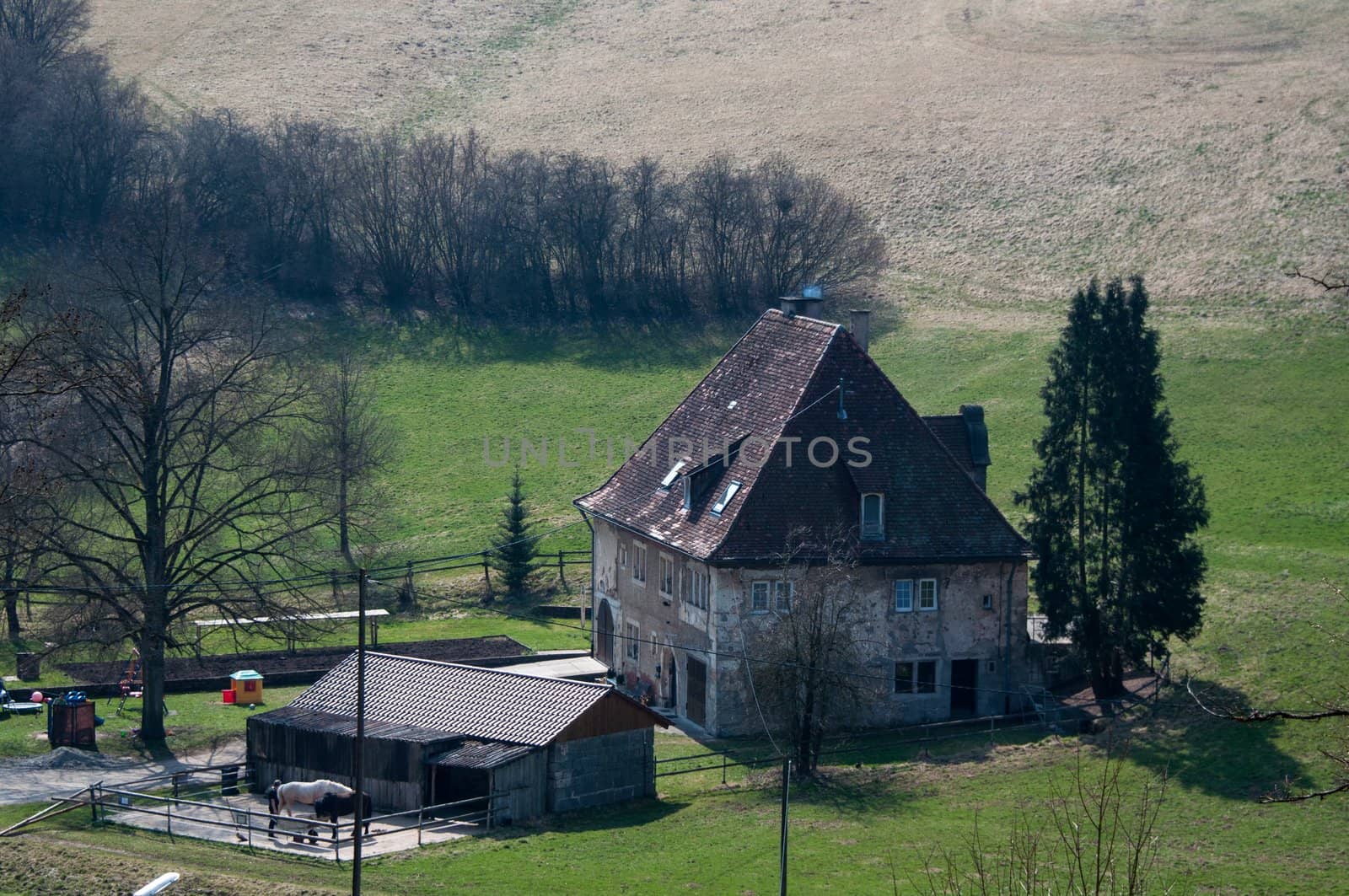 A large old farmhouse with horses and stable surrounded by fields and meadows