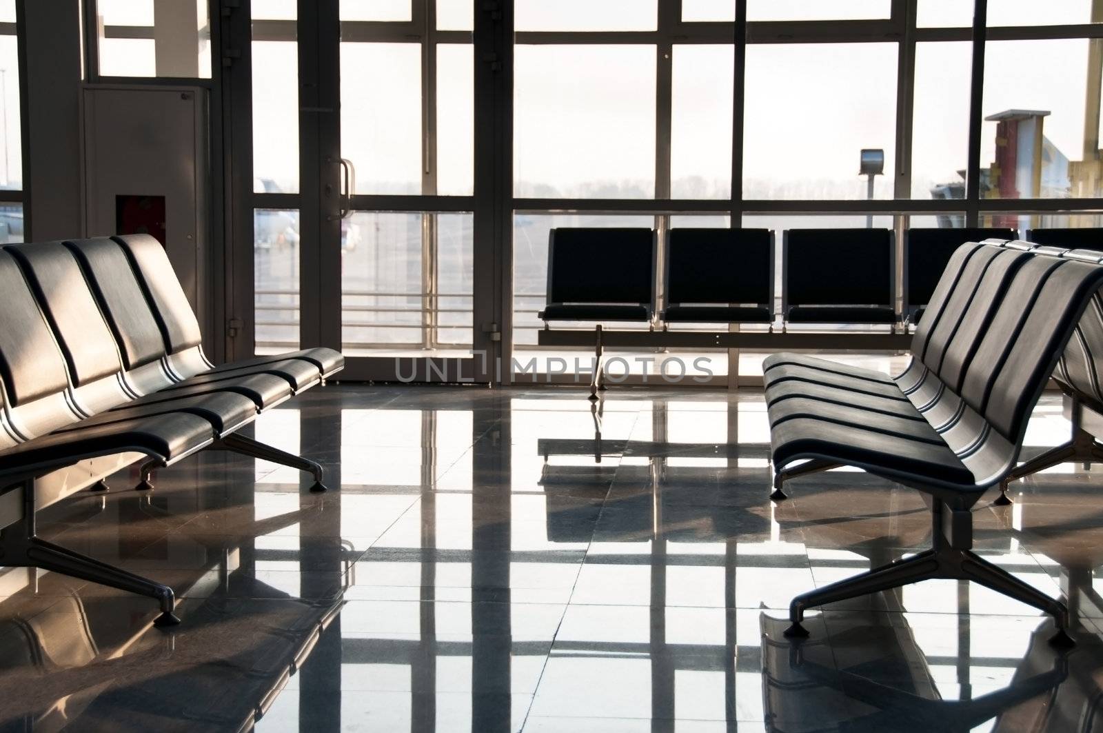 Rows of empty sits and big window in an airport. Focus on the front.