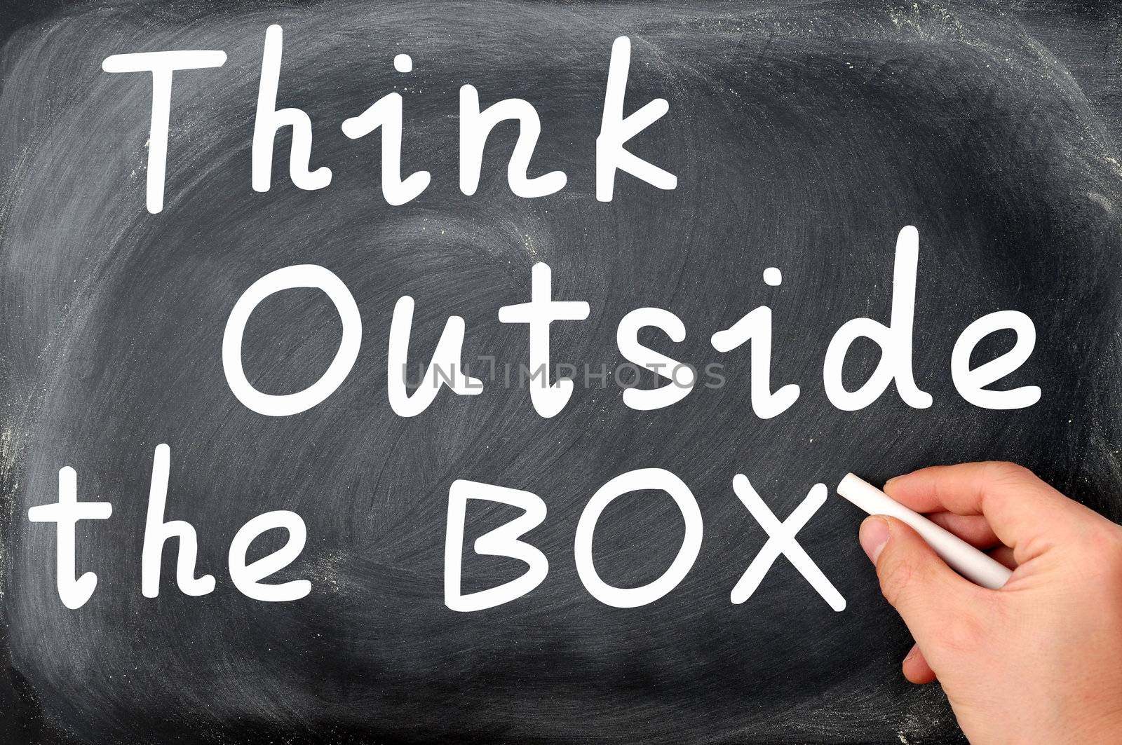 Think outside the box written on a Blackboard background with a hand holding chalk