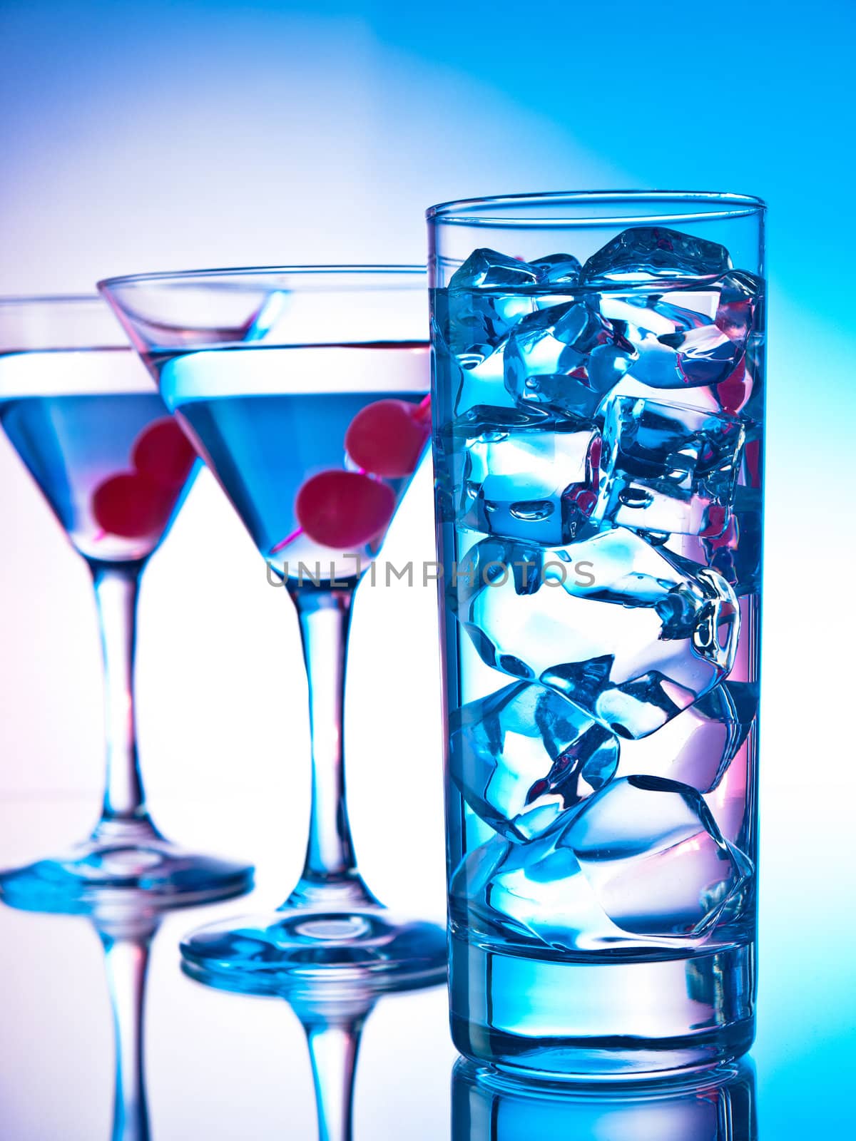 Two glasses of martini with red cherries and a glass of clear cocktail