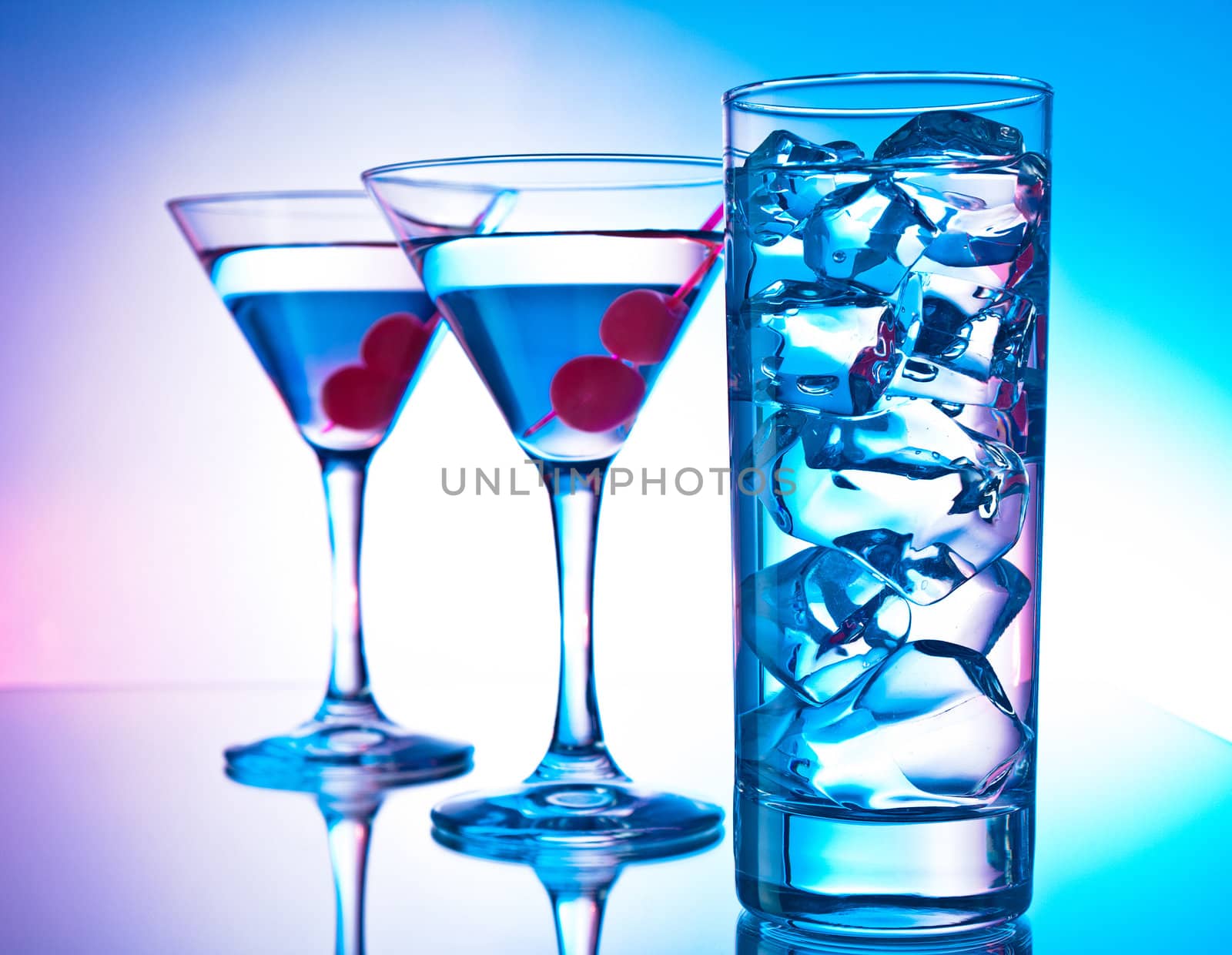 Two glasses of martini with red cherries and a glass of clear cocktail