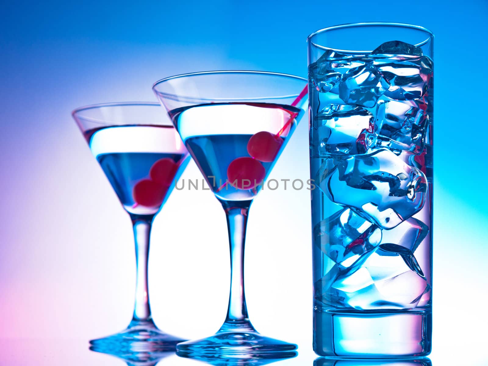 Two glasses of martini with red cherries and a glass of clear cocktail