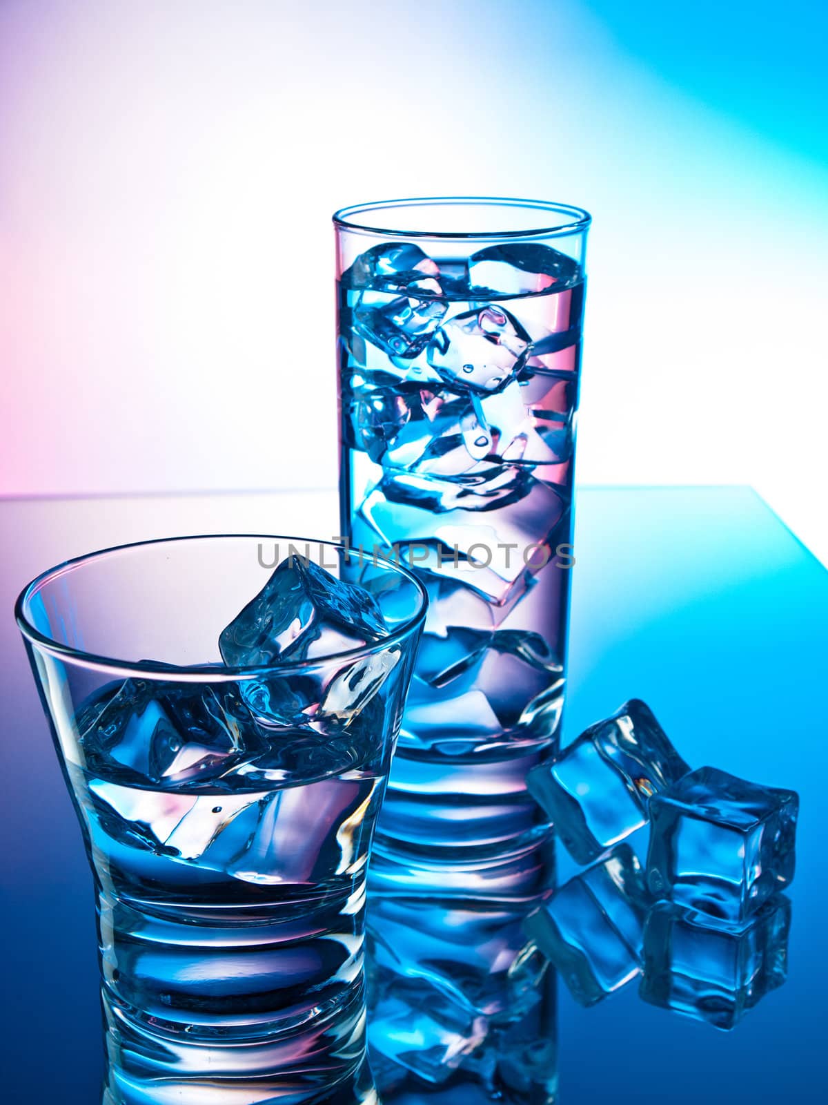 Two cocktails on a reflective surface with ice cubes