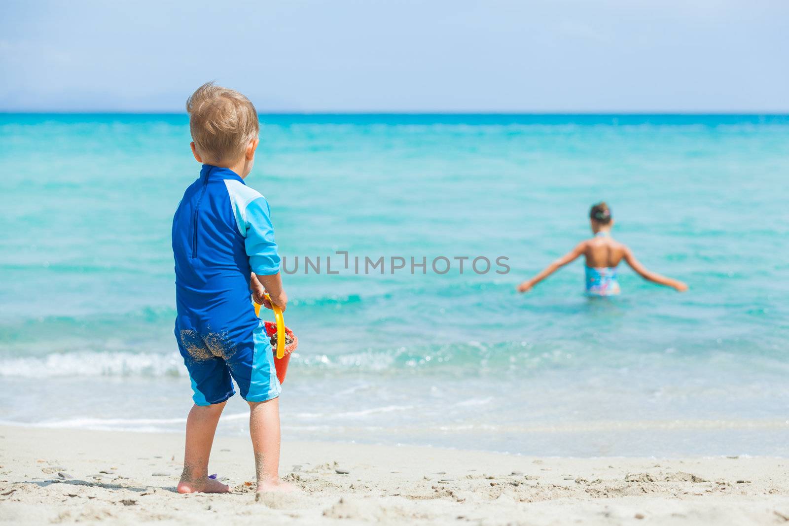 Back view young boy on sandy tropical beach, his sister background.