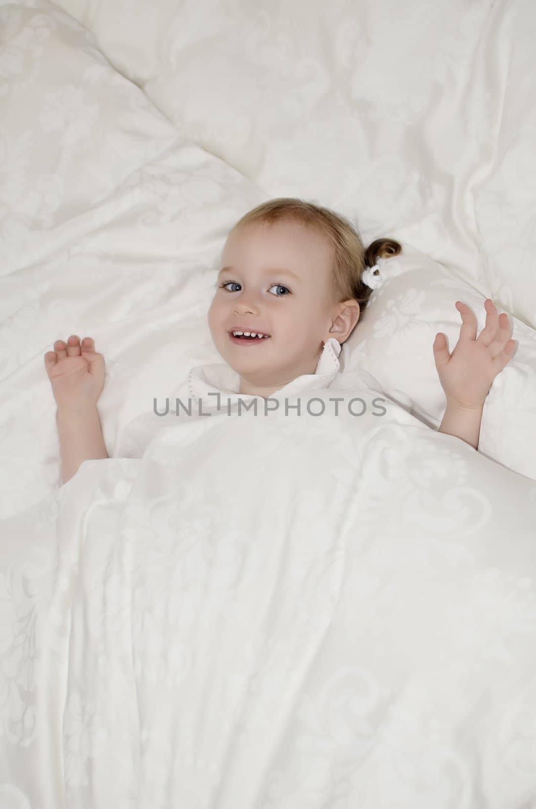 Funny little girl lying on the bed under the covers.