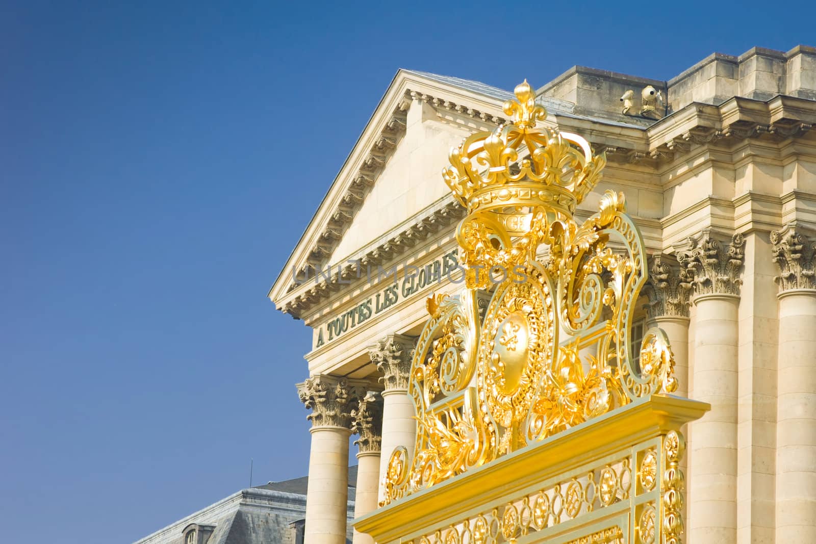 Golden crown over the gate and Palace in Versailles over blue sky. France