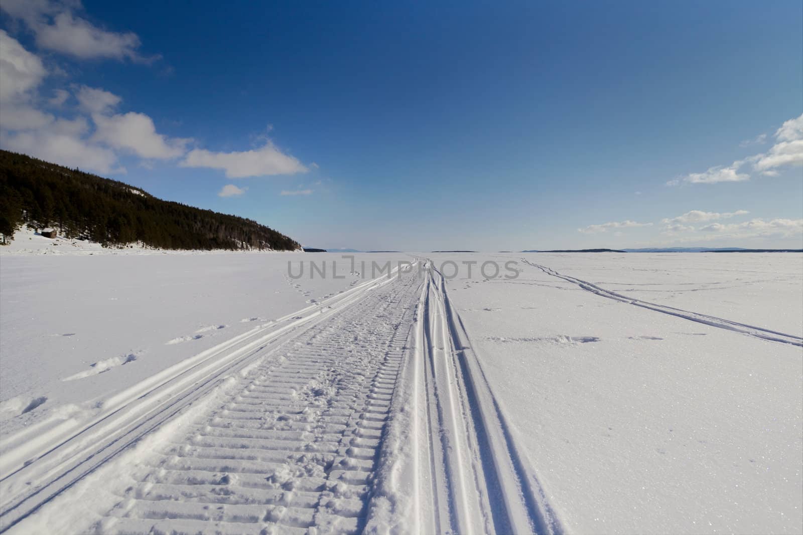 Snowmobile trail stretching into the distance against the blue sky and snowy expanses