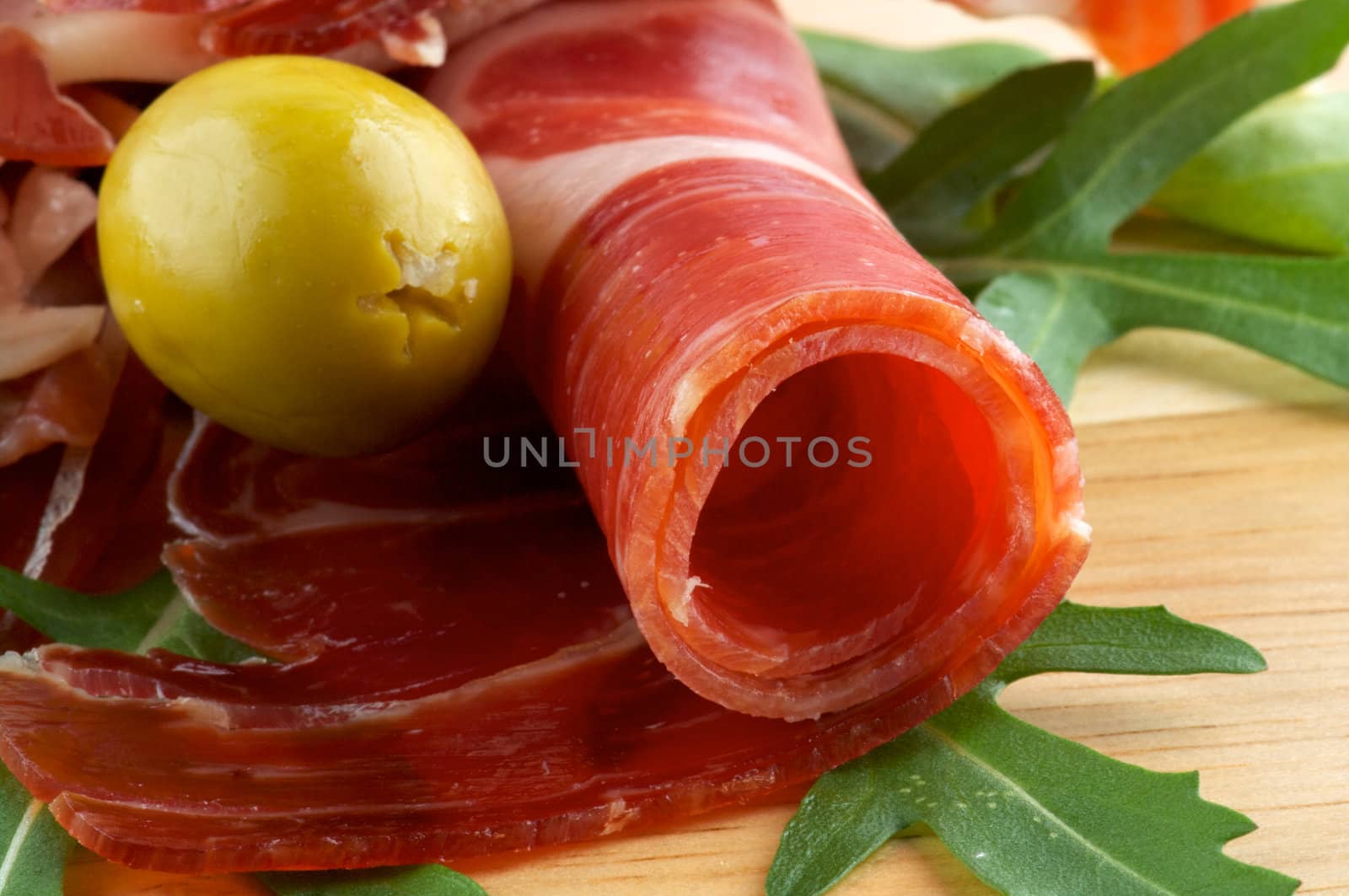 Slices of jamon and olives close up on wooden background