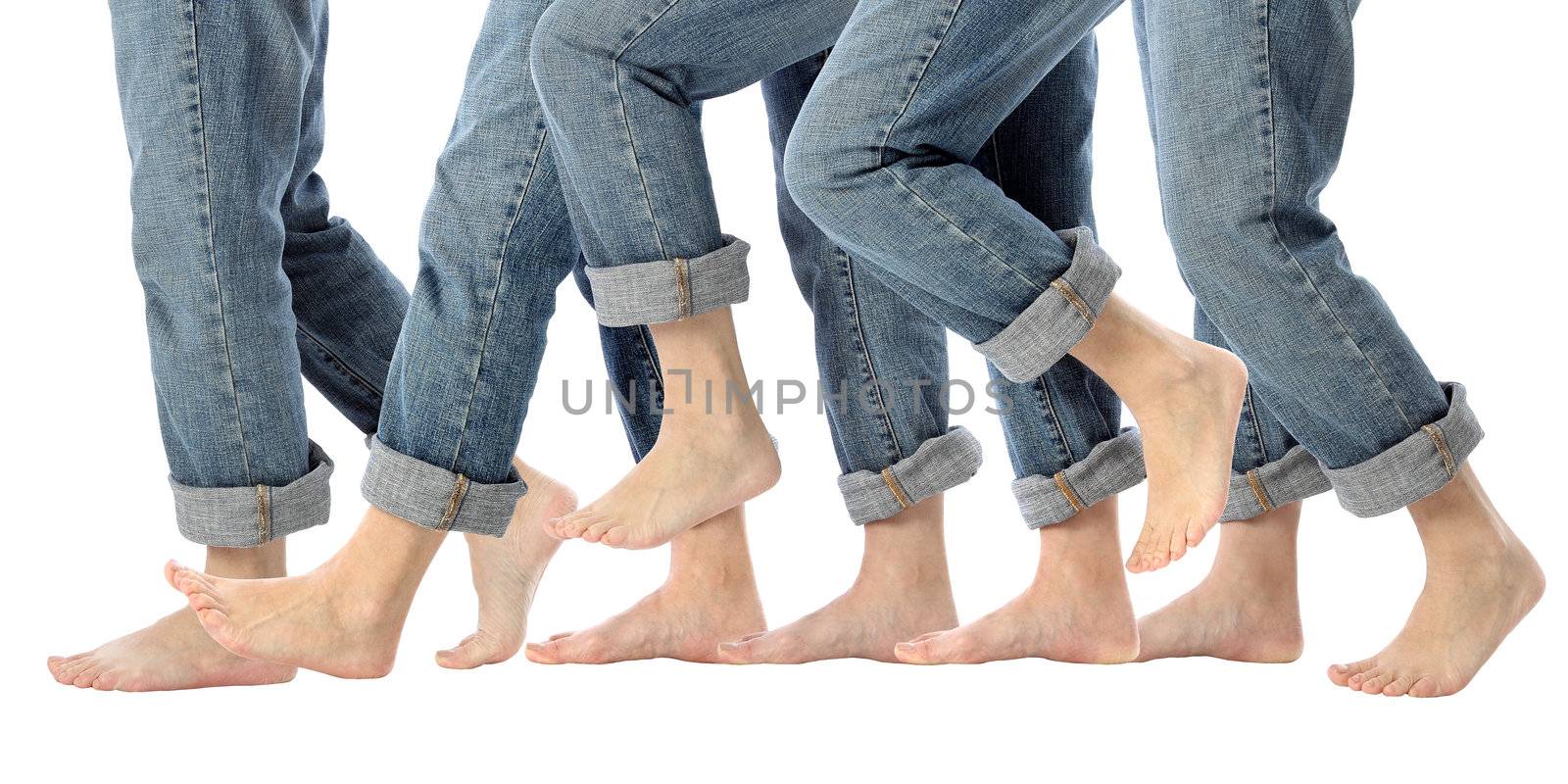A womans bare feet advance one step forward in rolled up jeans on white