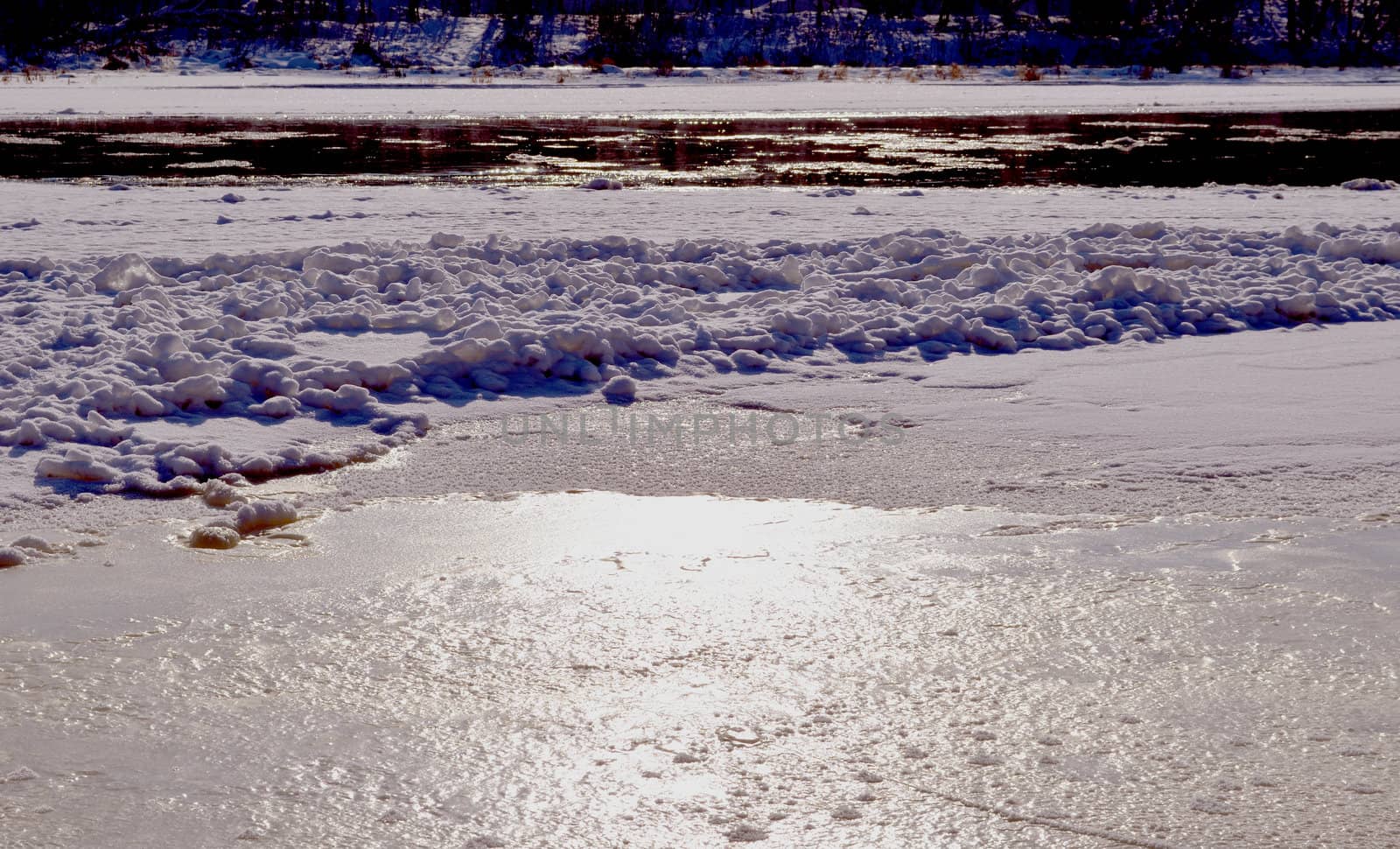 Partially frozen but still flowing river, and floe carried by water. Natural sun reflections.