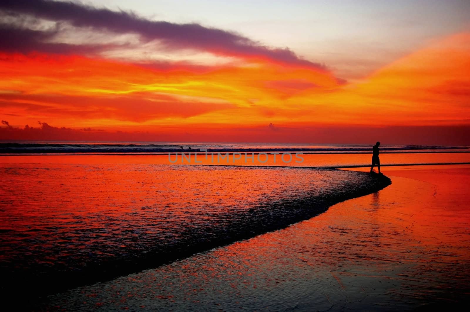 Silhouette of man in distance walking on beach at sunset, Bali.
