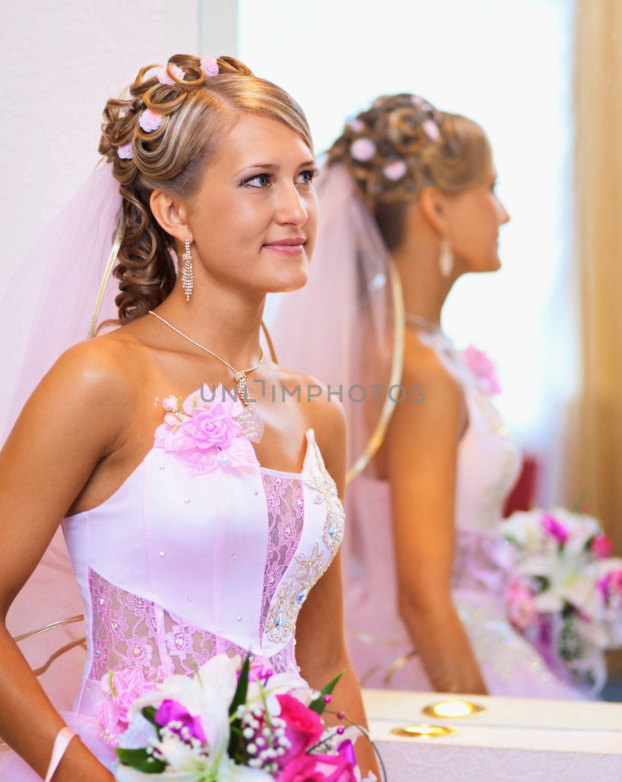 Portrait of a beautiful bride in a pink dress near the mirror