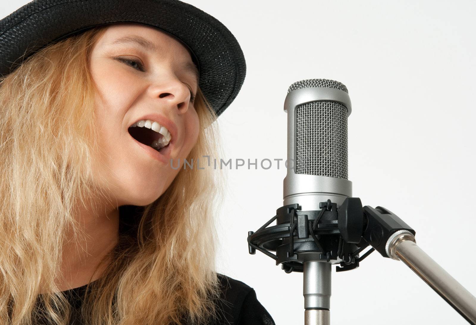 Young woman in black hat singing with studio microphone. Isolated on white background.