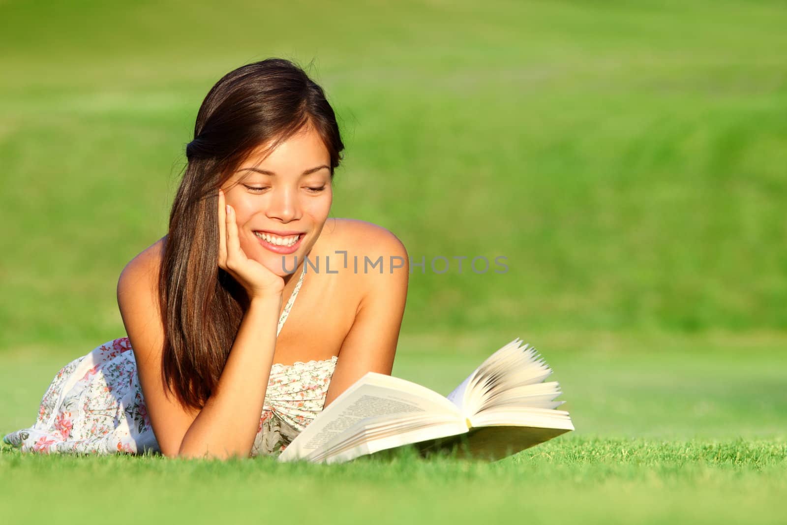 Reading. Woman reading book in park during spring / summer time. Happy smiling beautiful young university student studying lying down in grass. Beautiful mixed race Asian Chinese / Caucasian female model outdoors.