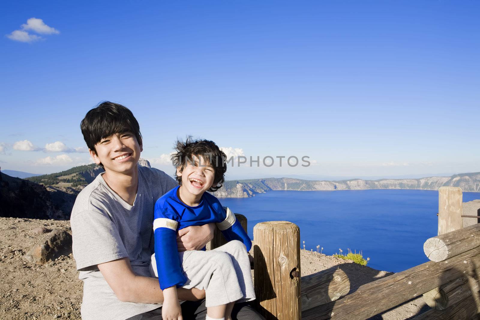 Big brother holding smiling disabled little boy with Oregon's famous Crater Lake in the bakcground. Child has cerebral palsy