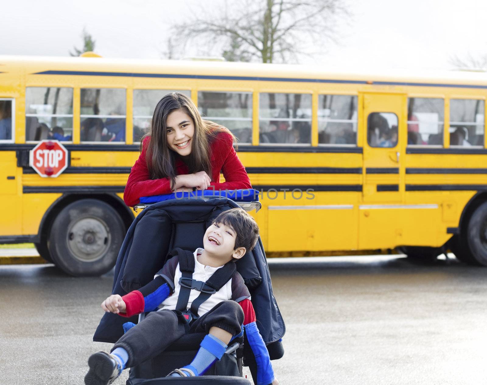 Big sister with disabled brother in wheelchair by school bus by jarenwicklund