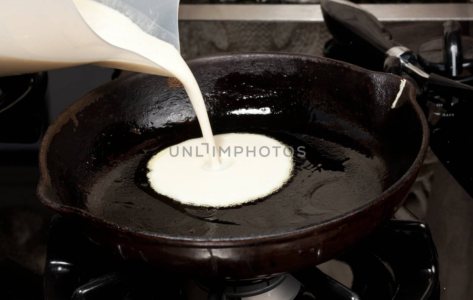 Frying pan on gas stove with pancake mixture being cooked