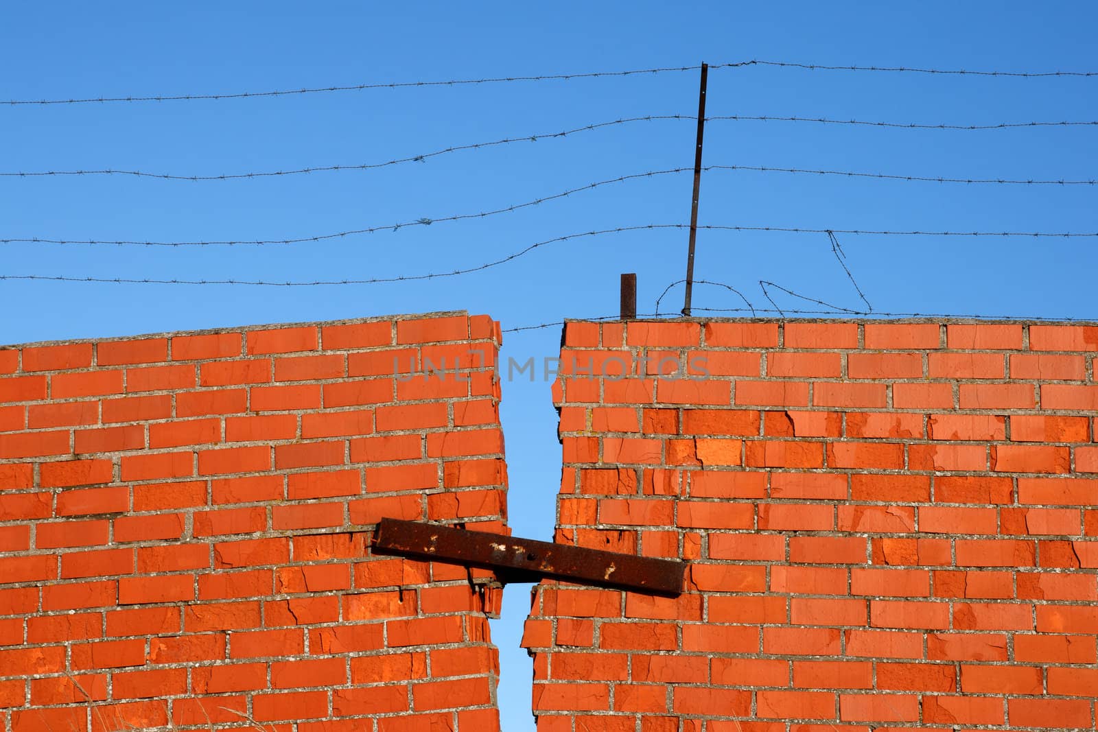 Red Brick broken Wall with barbed wire against blue sky
