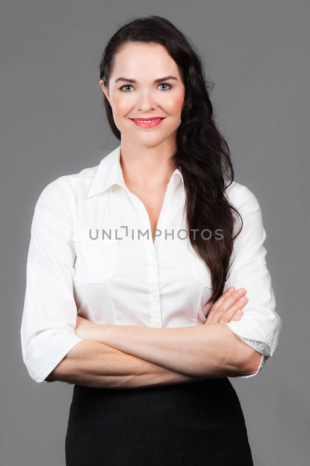 Portrait of a happy young business woman with arms folded, over grey background