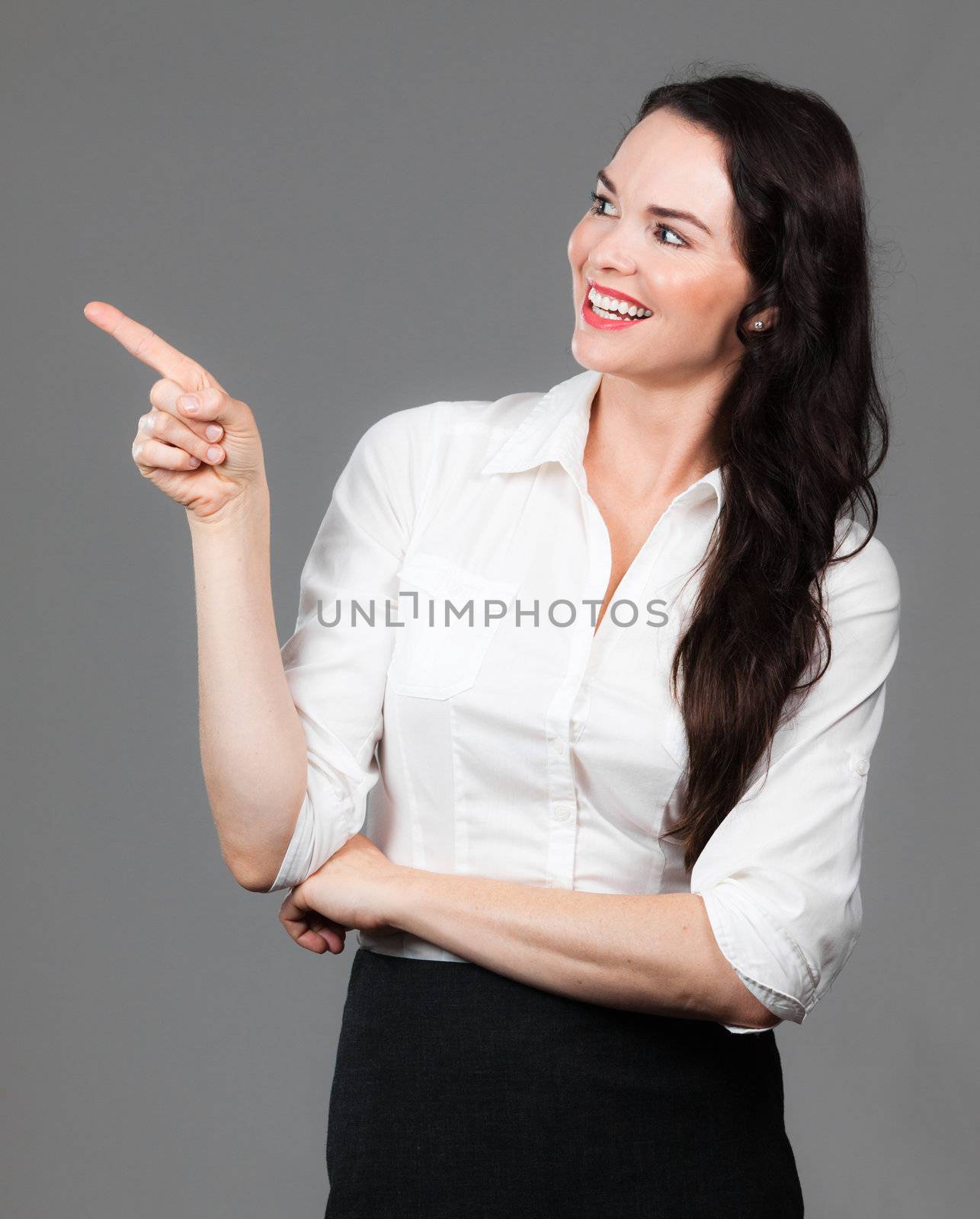 A happy beautiful business woman pointing and looking at copyspace, over grey background