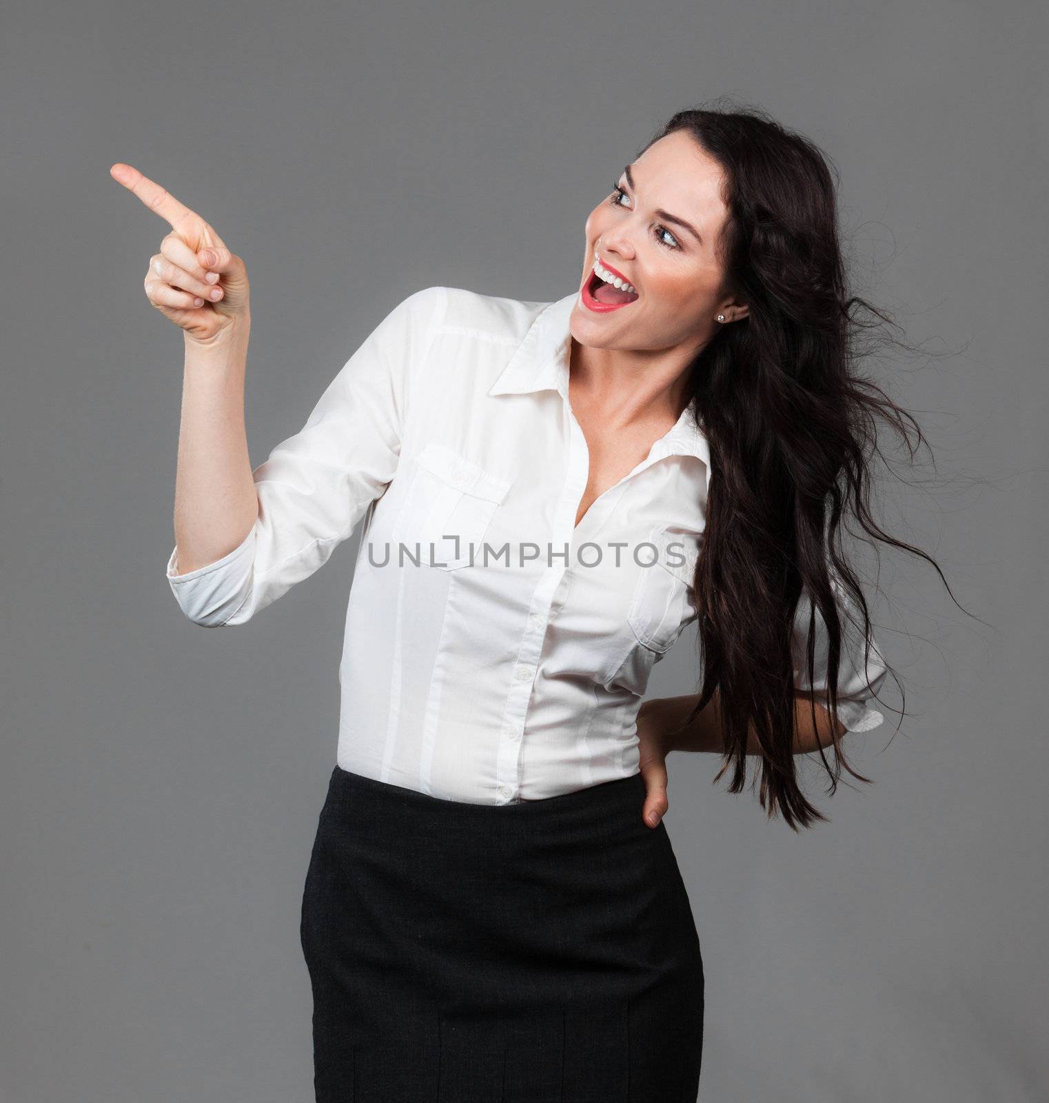 A cheerful beautiful business woman pointing and looking at copyspace, over grey background