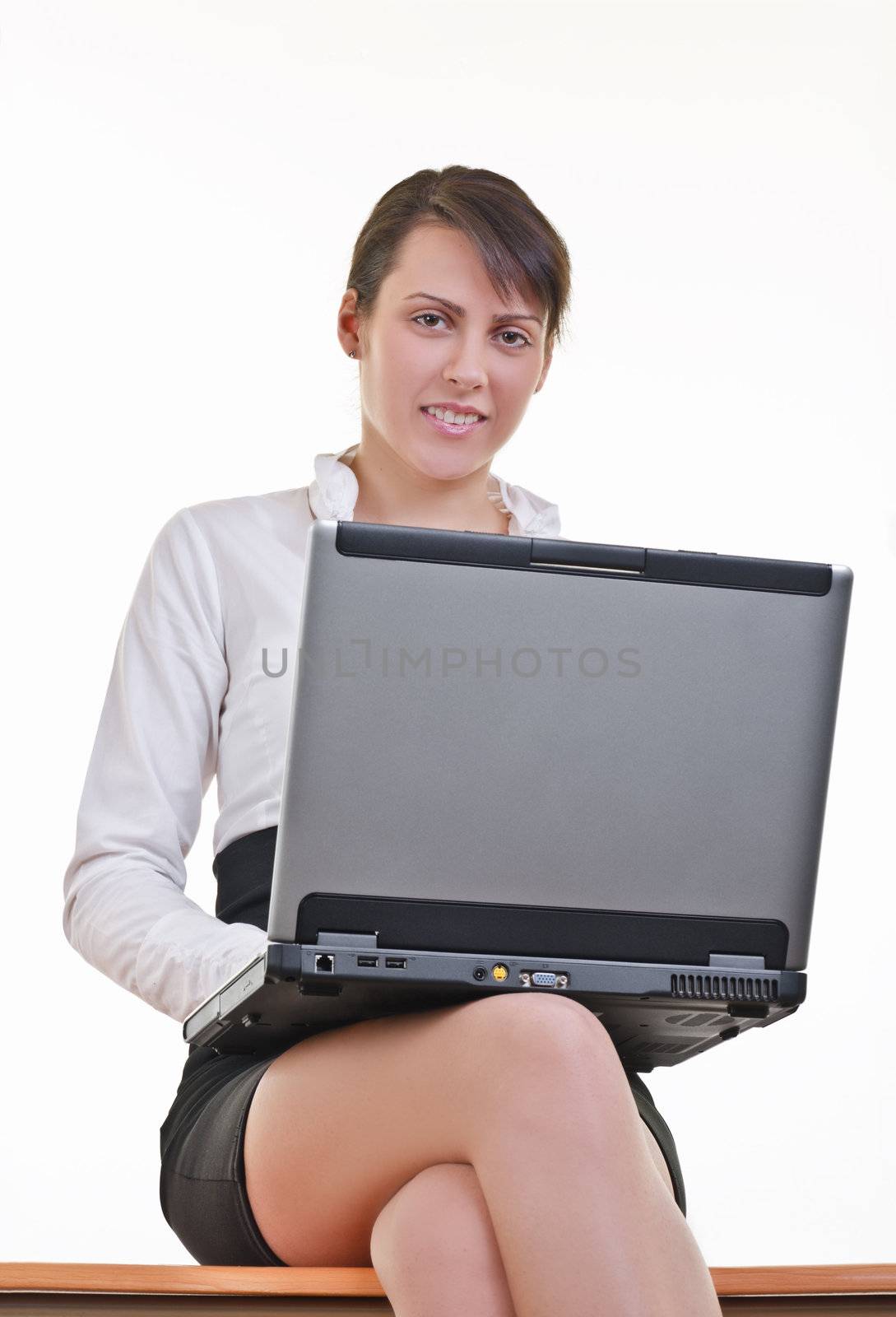 Office assistant in mini-skirt and white shirt sitting on top of office desk with laptop, eye contact