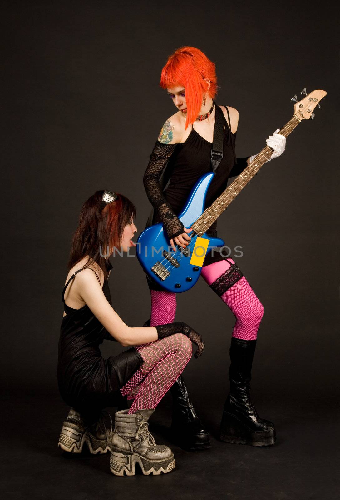 Two rock girls, one of them licking guitar, isolated on black background