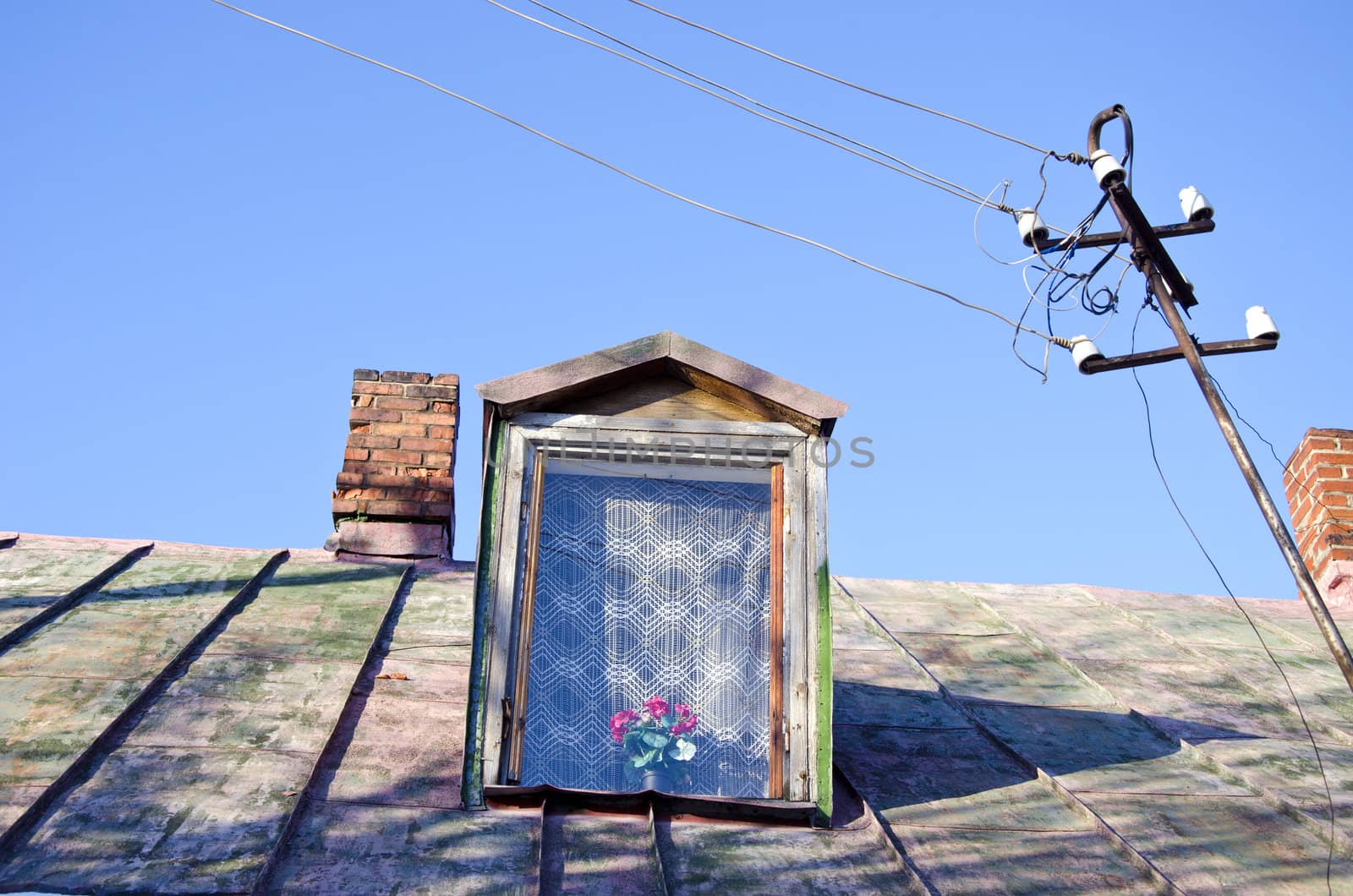 Ancient rural village house tin roof and attic window and chimneys. Tangled electrical wires.