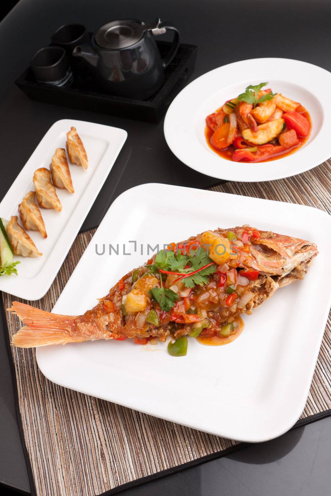 Freshly prepared Thai style whole fish red snapper dinner with sweet and sour shrimp and pan fried gyoza dumplings appetizer.  
