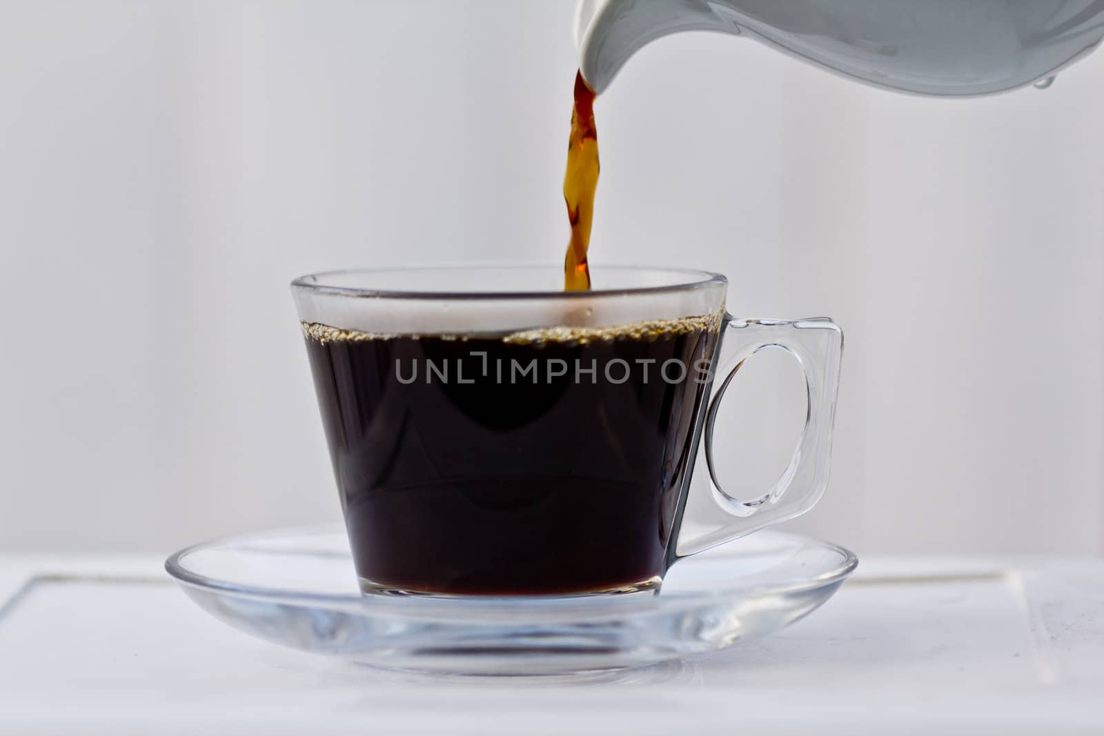 Pouring coffee into an almost full clear cup with a saucer.