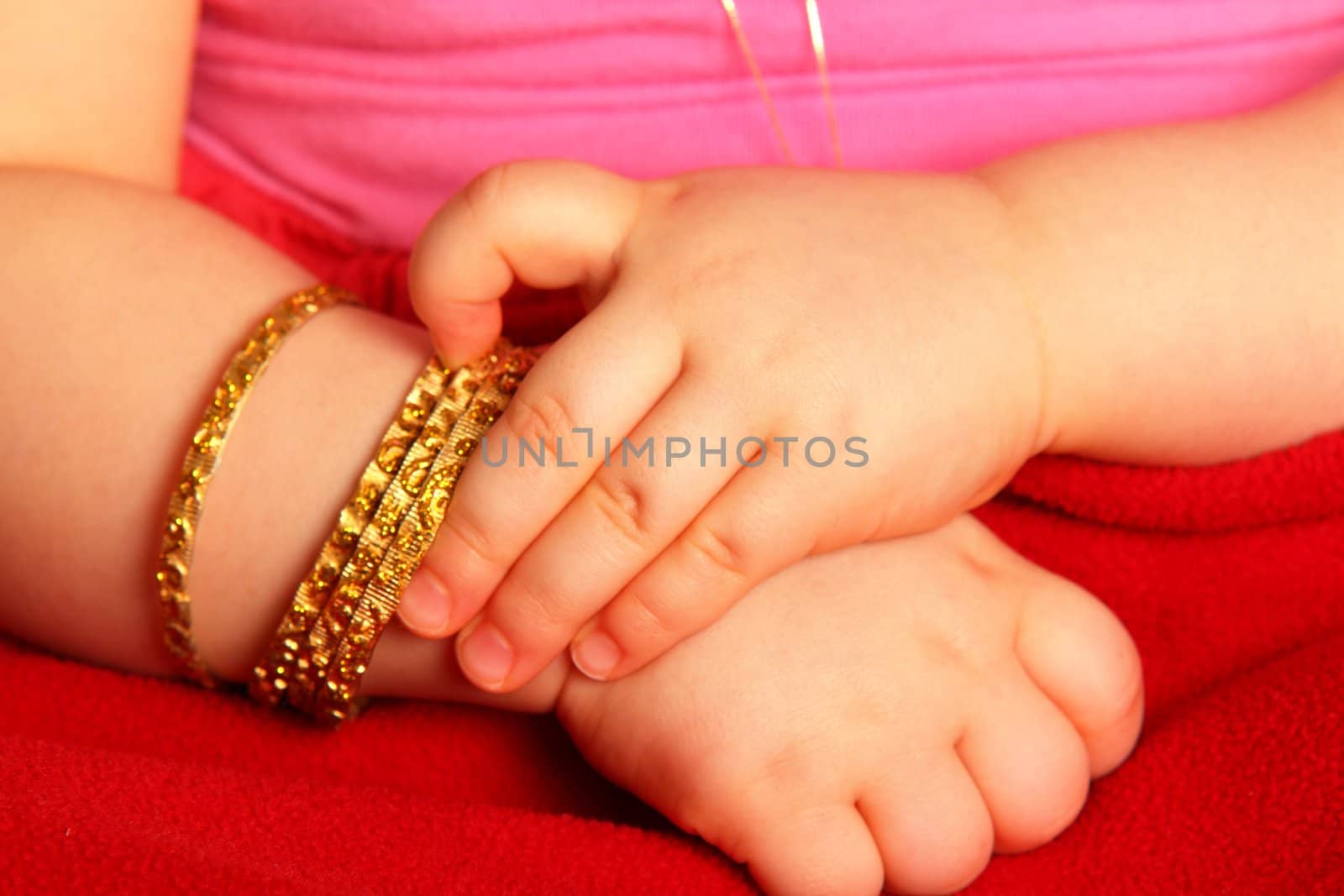 Baby hands, with a golden bracelet, isolated towards dark red