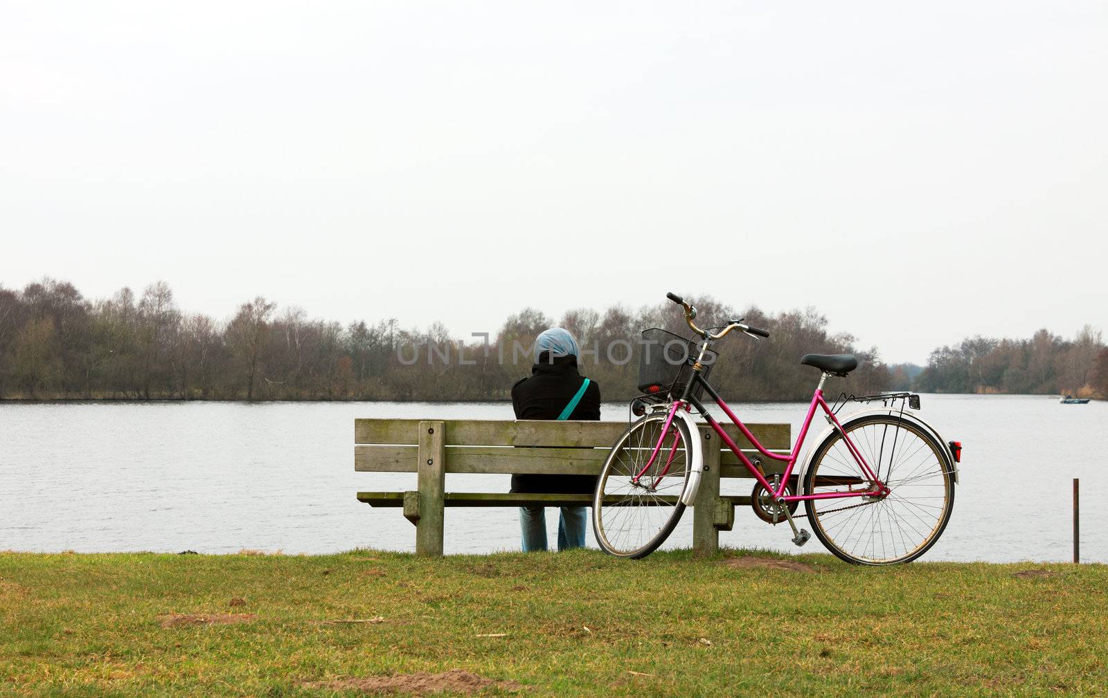 lonely girl on the bench close to the lake and bicycle